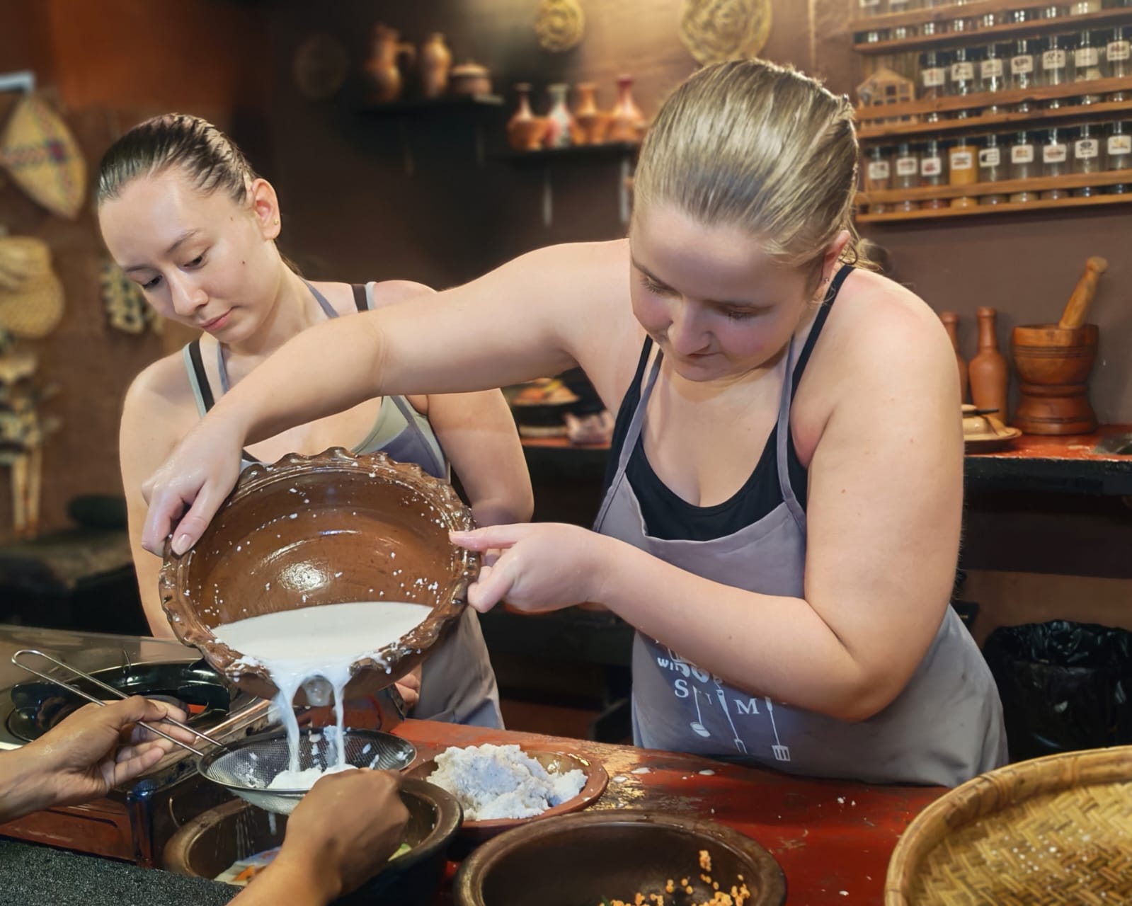 Guests pouring and straining fresh hand-squeezed coconut milk into clay pot